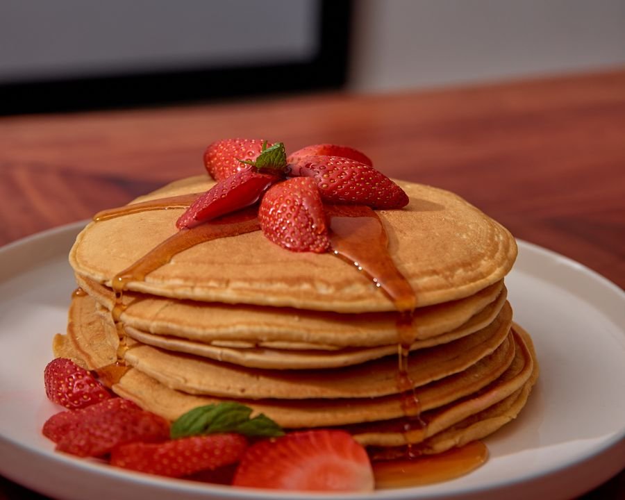 A tall stack of pancakes with syrup and strawberries