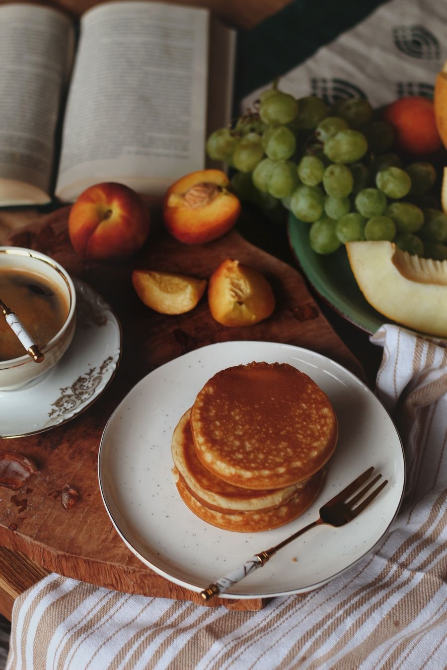 A small stack of thin pancakes on a plate beside coffee and fruit